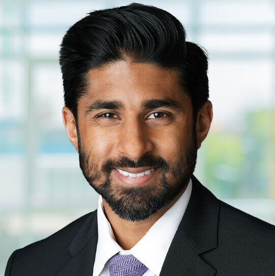 Haseeb, a man with black hair and a beard, wears a white shirt, purple tie and black jacket.