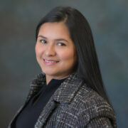Johana, a woman with dark brown hair, wears a black blouse and tweed blazer. 