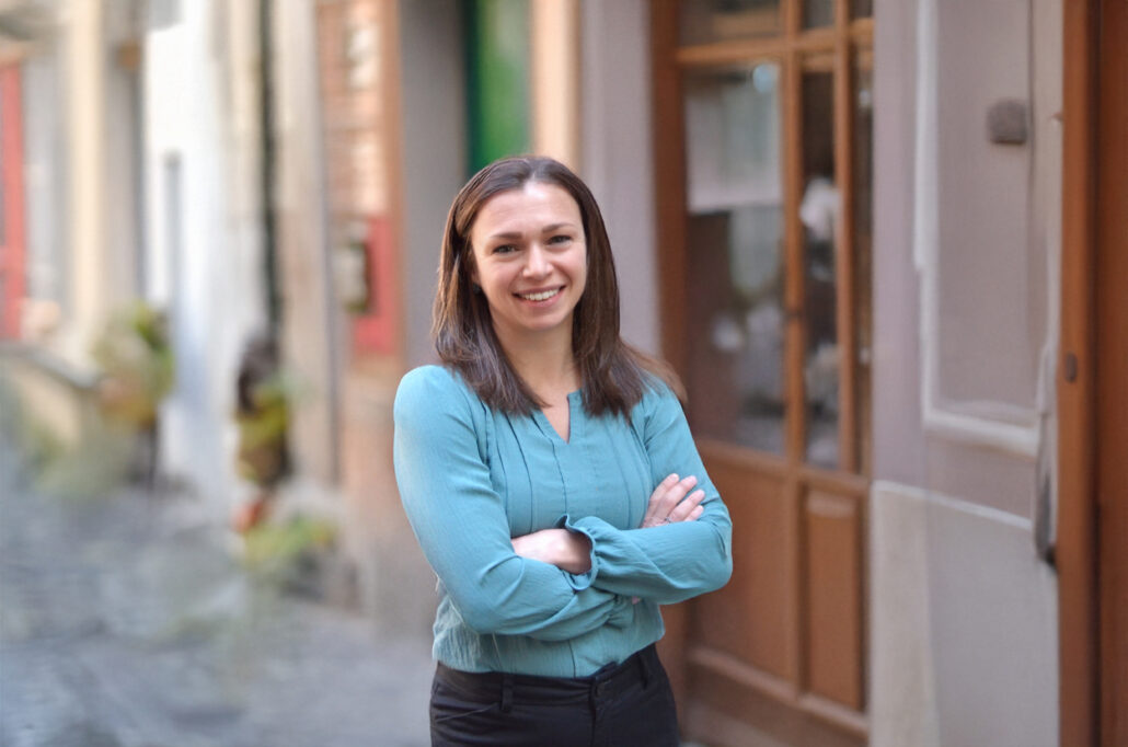 Natalia, a white woman with brown hair, wears a light blue blouse.
