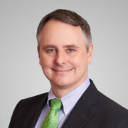 Iain, a white man with brown hair, wears a light blue shirt, green tie and black blazer.