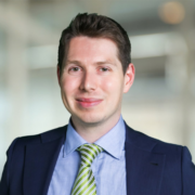 John, a white man with black hair, wears a pale blue shirt, lime green tie and navy blazer.