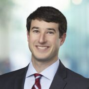 Jonathan, a white man with brown hair, wears a white shirt, red tie and black jacket. 
