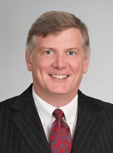 Julian, a white man with grey hair, wears a white shirt, red tie and black jacket.