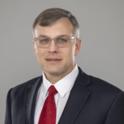 Todd, a white man with brown hair, wears a white shirt, red tie and navy blue suit. 