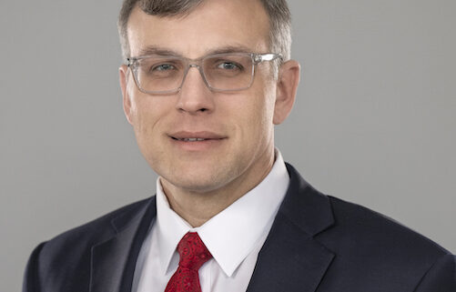 Todd, a white man with brown hair, wears a white shirt, red tie and navy blue suit.
