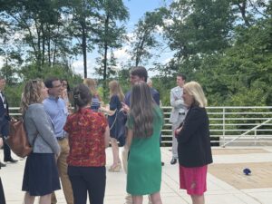 Isley is pictured in the middle of the photo wearing a suit. He stands talking with other attendees outside the bar center. There are trees behind them.