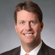Philip, a white man with brown hair, wears a white shirt, black suit and yellow tie.