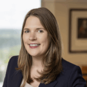 Anna, a white woman with light brown hair, wears a white blouse and black blazer.