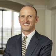 Ben, a white man with brown hair, wears a white shirt, yellow and grey tie and grey suit.