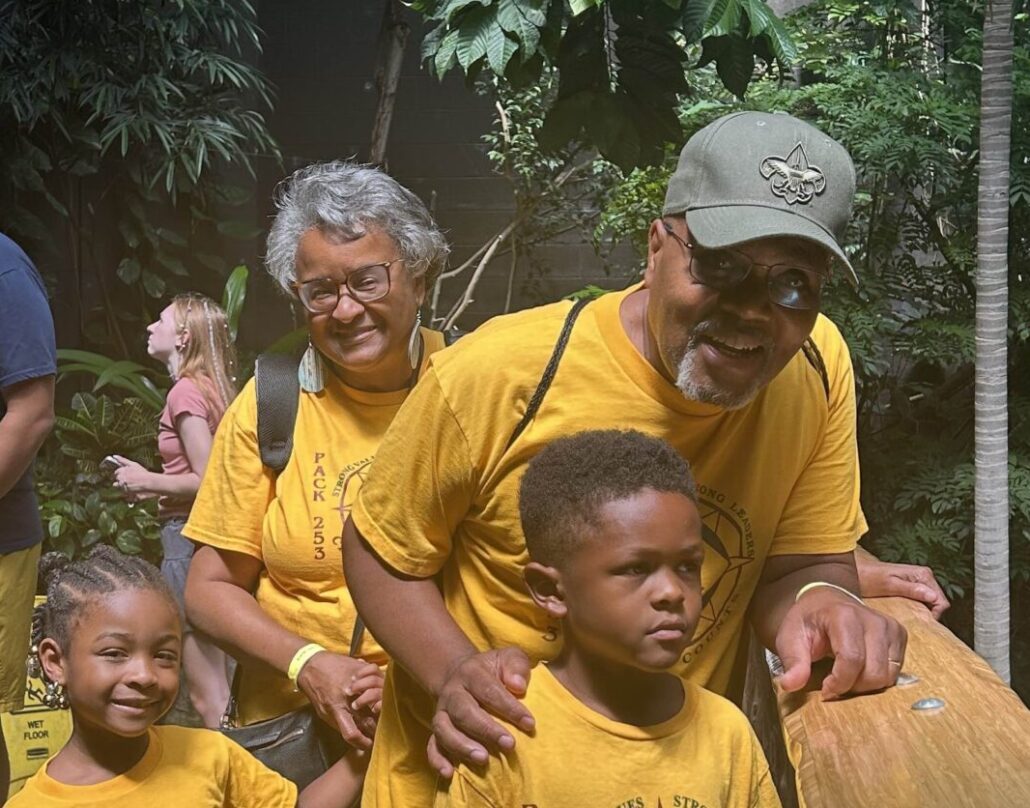 Bernice, a Black woman with grey hair, is pictured with her husband, granddaughter and grandson outside on a bridge at Carowinds.