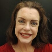 Sarah, a woman with brown hair, wears a burgundy blouse and gold necklace.