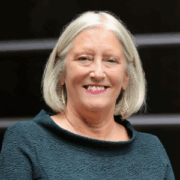 Deb, a white woman with grey blonde hair, wears a teal dress. 