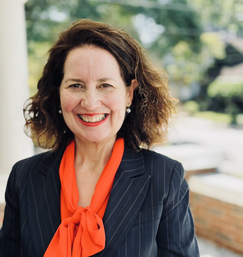 Meredith, a white woman with brown hair, wears a bright orange blouse and a black jacket.