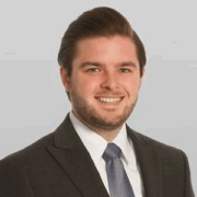 Nick, a white man with brown hair, wears a white shirt, dark grey tie and grey suit. 
