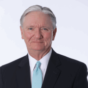 Ralph, a white man with grey hair, wears a white shirt, blue tie and black suit.