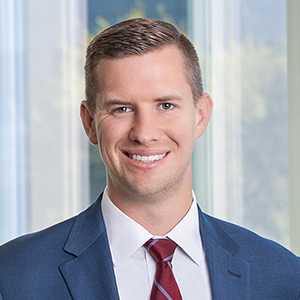 Ryan, a white man with light brown hair, wears a white shirt, red tie and navy suit.