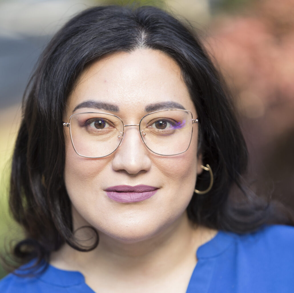 Sofia, a woman with dark brown hair and brown eyes, wears a blue blouse and glasses.