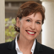Maria, a white woman with brown hair, wears a white shirt and black blazer.