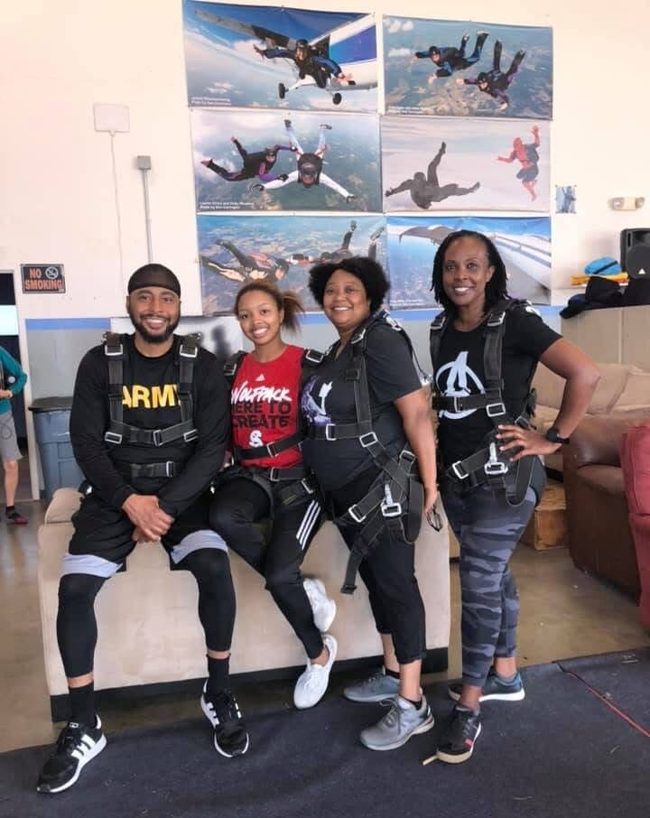 Yolanda and her family are pictured in skydiving gear, and they are smiling.