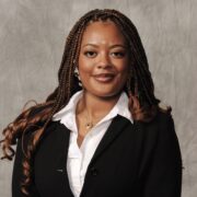 Aaliyah, a Black woman with auburn and brown hair, wears a white blouse and black suit.