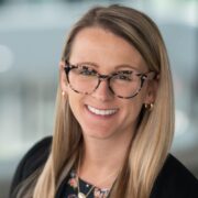 Melissa, a white woman with blond hair and brown glasses, wears a floral blouse and black suit.