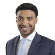 Gaaron, a man with black hair, wears a white shirt, pale blue tie and grey suit.