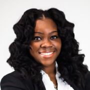 Brittany, a black woman with wavy black hair, wears a white blouse and black blazer. 