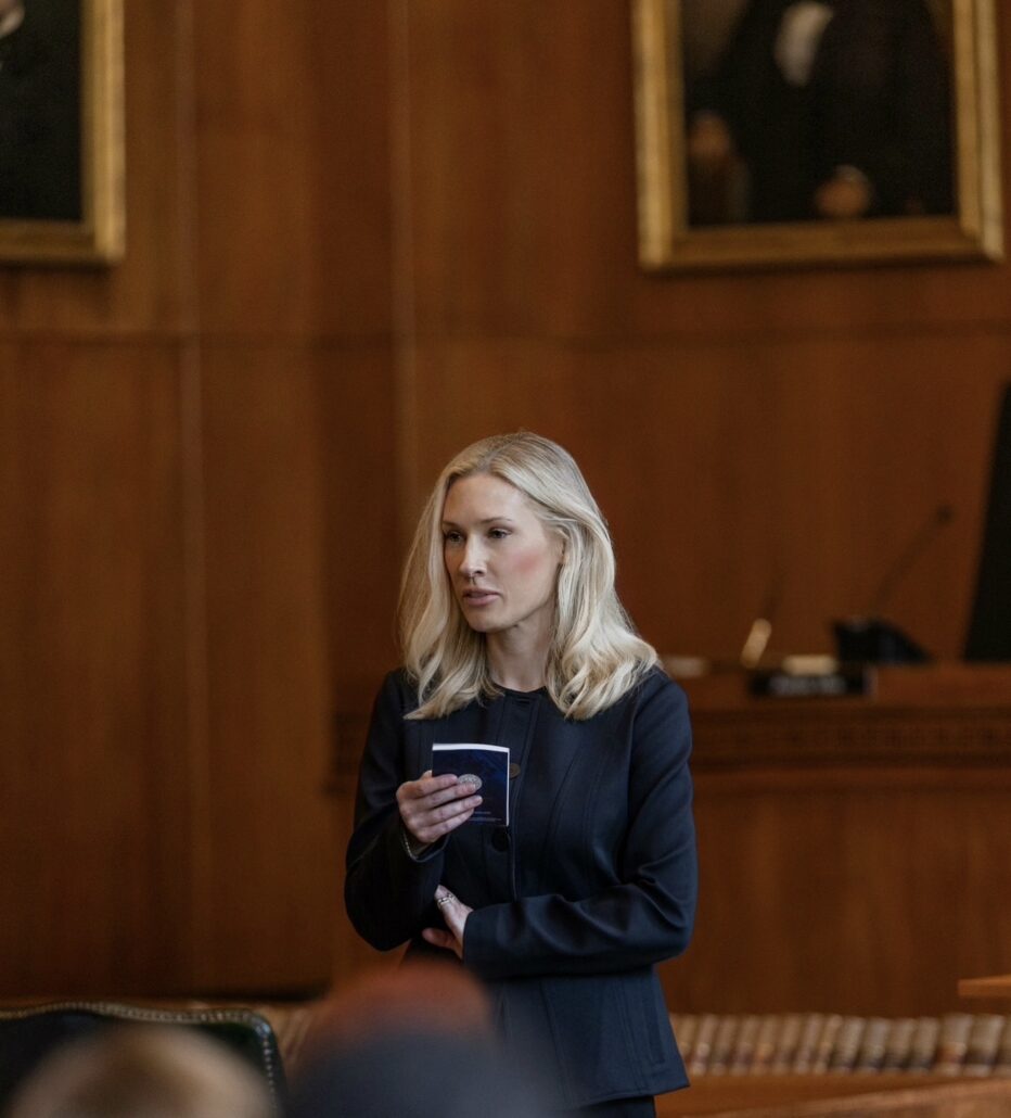 Judge Skeens, a white woman with blond hair, wears a black suit and stands speaking in a courtroom.