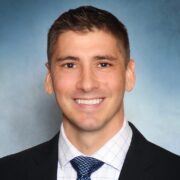 Jason, a white man with brown hair, wears a white shirt, blue tie and black jacket.