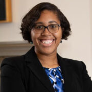 Taylor, a Black woman with black hair, wears a blue and white blouse and black jacket.