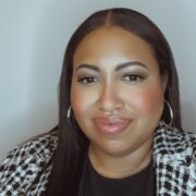 Alex, a Black woman with black hair, wears a black blouse and a blazer with black and white checks.