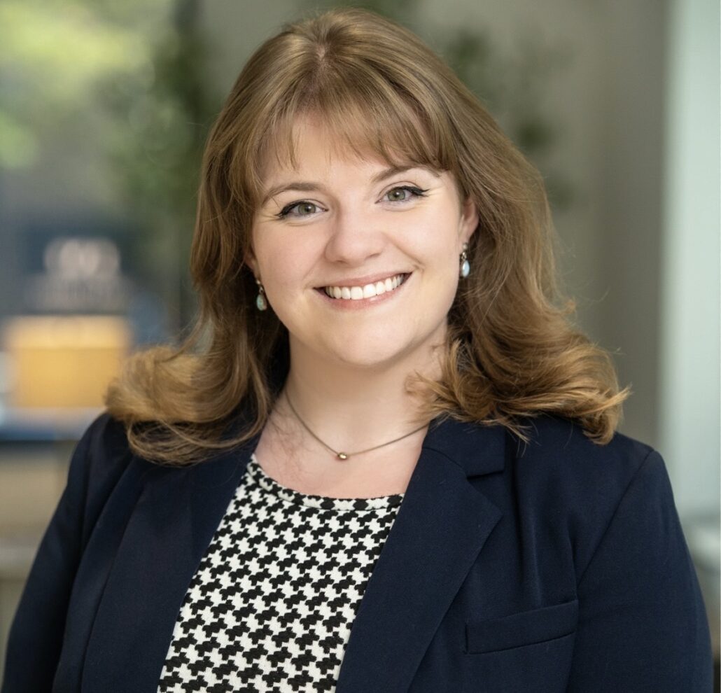 Courtney, a white woman with light brown hair, wears a dress with a black and white checkered pattern and a black blazer.