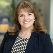 Courtney, a white woman with light brown hair, wears a dress with a black and white checkered pattern and a black blazer.