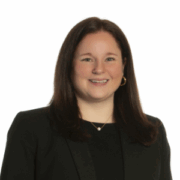 Catherine, a white woman with brown hair, wears a black blouse and black blazer. 