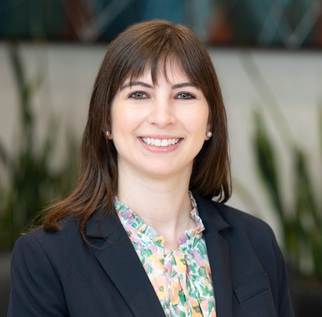 Maya, a white woman with brown hair, wears a floral blouse and black blazer.