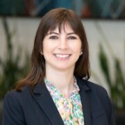 Maya, a white woman with brown hair, wears a floral blouse and black blazer.