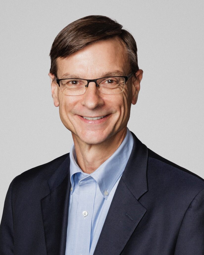 Phil, a white man with brown hair and glasses, wears a blue shirt and black blazer.