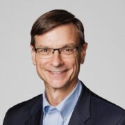 Phil, a white man with brown hair and glasses, wears a blue shirt and black blazer.