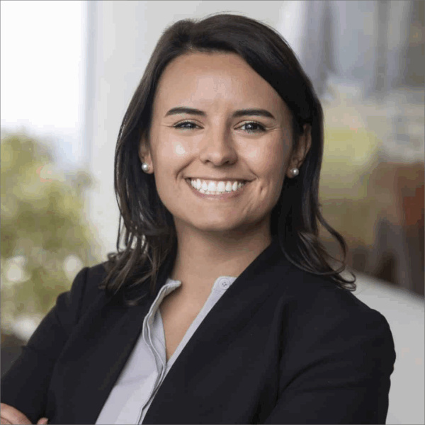 Clare, a white woman with shoulder-length brown hair, wears a grey button-down shirt, black jacket and pearl earrings.