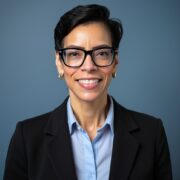 Stacey, a woman with black hair and black glasses, wears a blue button-down shirt and black blazer.