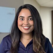 Huma, a woman with brown hair, wears a dark purple button-down blouse.