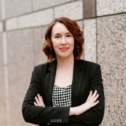 Ashley, a white woman with brown hair, wears a black and white blouse and black blazer. 