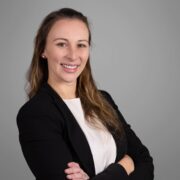 Anastasia, a white woman with brown hair, wears a white blouse and black jacket. 