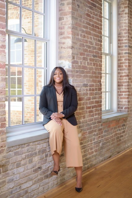 Judge Taylor is a Black woman with dark brown hair. She wears a light tan jumpsuit, a black jacket and a pearl necklace.