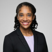 Jasmine, a Black woman with black hair, wears a light purple blouse with a black suit. 