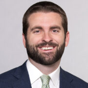 Curtis, a white man with brown hair and a beard, wears a white shirt, green tie and black jacket.
