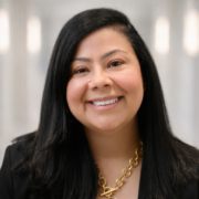 Diana, a woman with black hair, wears a white blouse, black blazer and gold necklace.