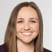 Katherine, a white woman with brown hair wears a black blouse and blazer.