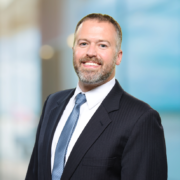 Landon, a white man with brown hair and a beard, wears a white shirt, blue tie and black jacket.