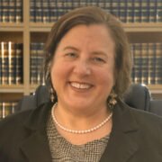 Kim, a white woman with brown hair, wears a grey blouse and black jacket.